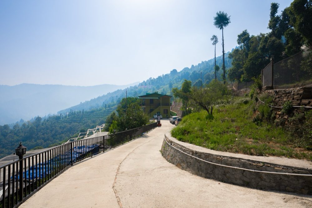 The paved approach road curving up to Erigeron Himalayan Hotel in Nathuakhan, with cars parked at the door