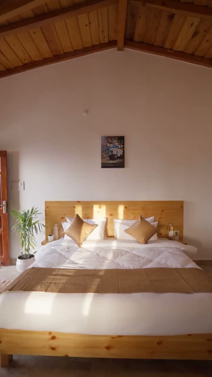 A bedroom under a pitched pine ceiling, morning sun falling across the bed