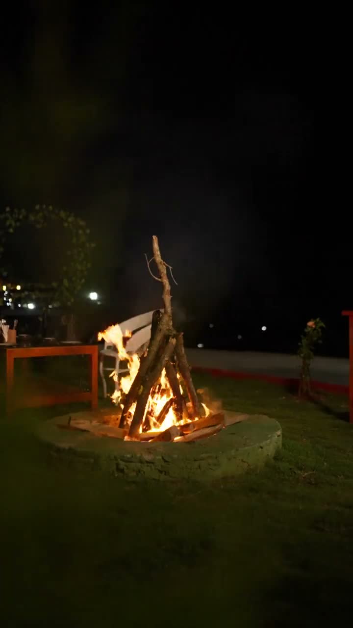 A bonfire burning in a round stone fire pit on the dark lawn, a ring of fairy lights behind it